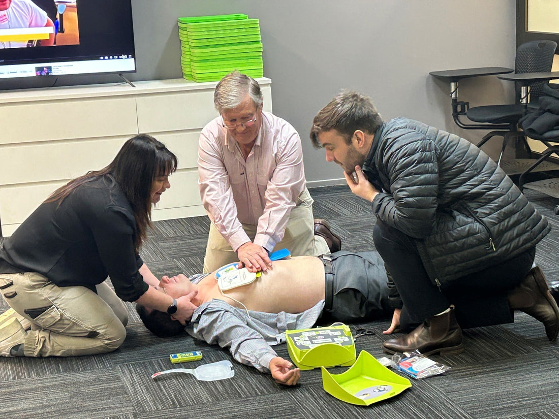 3 poeple performing CPR on a patient in cardiac arrest, using an AED in a training scenario for workplaces. By assurance First Aid Kits