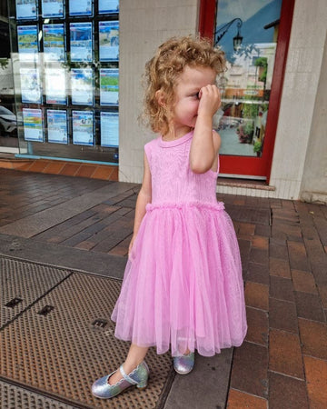 Child in a pink dress standing on a sidewalk with a building in the background