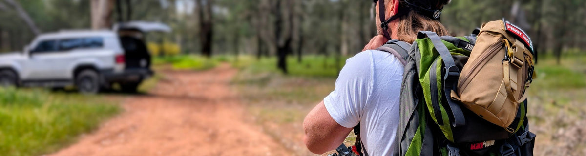 Man on a bike wearing a back pack with a snake bite kit attached.
