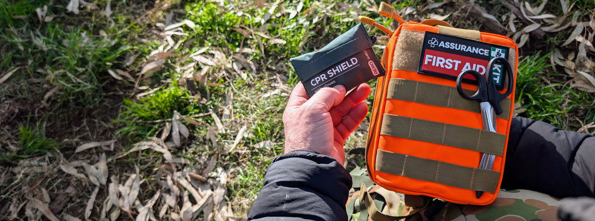 Hands holding  a hi vis orange snake & tick bite first aid kit.