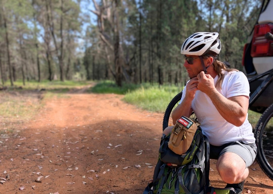 Man preparing to ride a bike, with a back pack and snake bite bandage